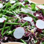 A colorful Balthazar salad with thinly shaved fennel, radicchio, and radishes, blanched asparagus, and haricots verts, drizzled with truffle-lemon dressing on a wooden salad bowl.
